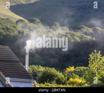 Smoking woodburner chimney on house in village, Wales, UK Stock Photo
