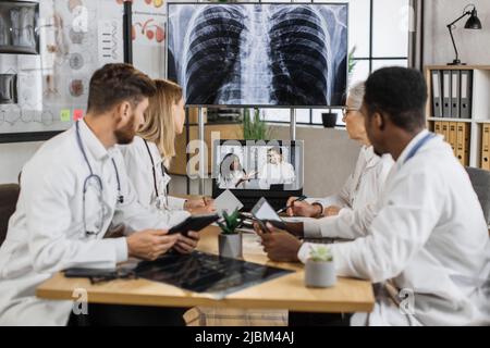Diverse team of medical scientist having online meeting with african american speaker about brain anomalies in high tech laboratory. Colleagues using laptop while sitting at table in neurology center. Stock Photo
