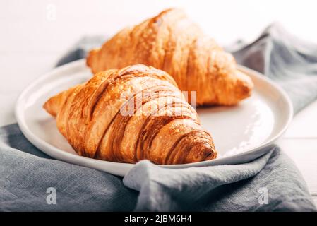 Plate with two fresh croissants on white table. Stock Photo