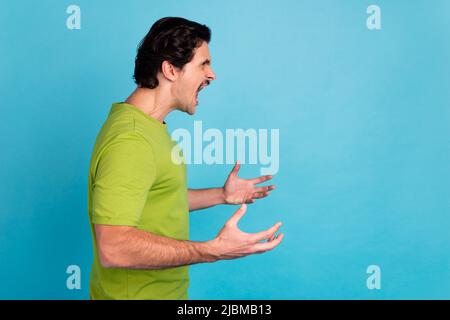 Photo of shocked angry man wear green t-shirt looking empty space screaming isolated blue color background Stock Photo