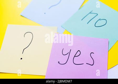 multicolored papers with yes and no lettering near question marks on yellow background Stock Photo