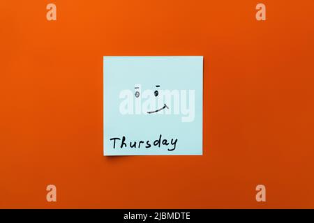 top view of sticky note with thursday inscription and positive smiley on orange background Stock Photo