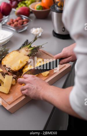 Unrecognizable man cutting a pineapple on chopping board. Stock Photo