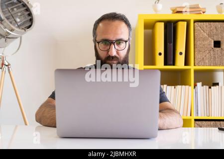 Working on laptop, front view of young man working on laptop. Modern office businessman working on computer sitting at table in office. Stock Photo