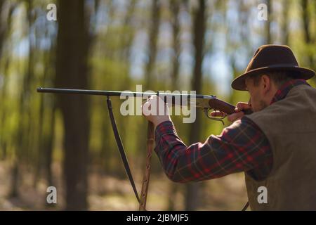 Hunter man aiming with rifle gun on prey in forest. Stock Photo