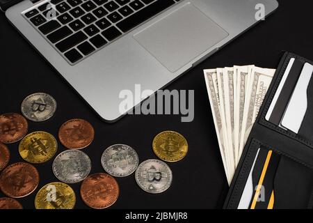 KYIV, UKRAINE - APRIL 26, 2022: Top view of wallet with money near laptop and bitcoins on black background Stock Photo