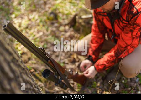 Hunter man with rifle gun waiting for prey in forest. Stock Photo