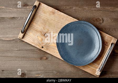 Dark ceramic plate and brown wooden tray on a brown wooden table. Layout for displaying dishes. Top view with copy space Stock Photo