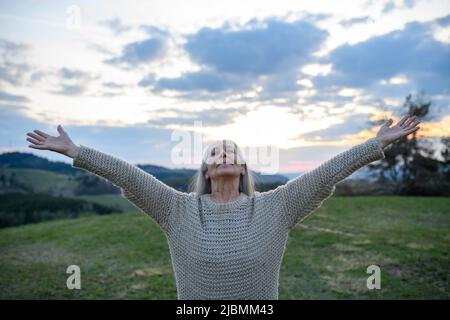 Senior woman with arms outstretched and face up at park on spring day Stock Photo