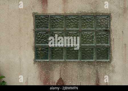 Old wall with the window made of translucen square glass tiles. Rough ribbed surface of green glass of window. Vintage texture for background and desi Stock Photo