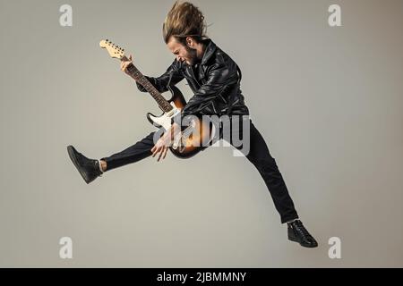 emotional bearded rock musician playing electric guitar in leather jacket and jumping, guitar player Stock Photo