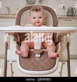 Happy baby with food stained mouth sitting on child chair, home kitchen background. Happy Baby (HB) - Moscow, Russia, January 26, 2022