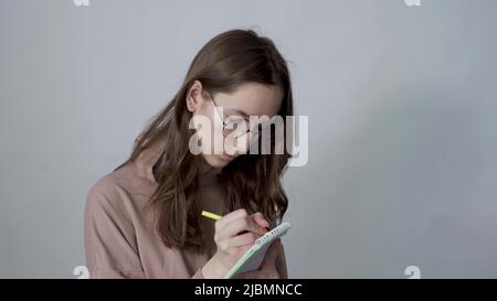 Young inspired woman pensively thinks and making notes in paper notebook Stock Photo