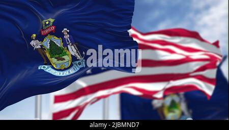 The Maine state flag waving along with the national flag of the United States of America. In the background there is a clear sky. Maine is a state in