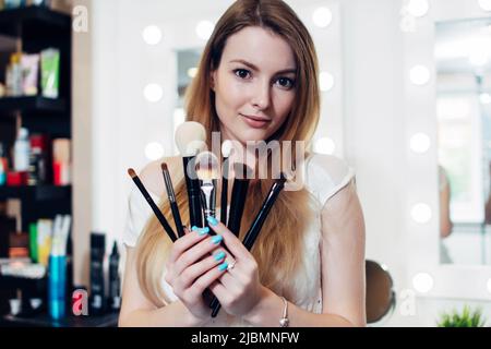 Portrait of female beautician holding a set of makeup brushes in beauty salon. Stock Photo