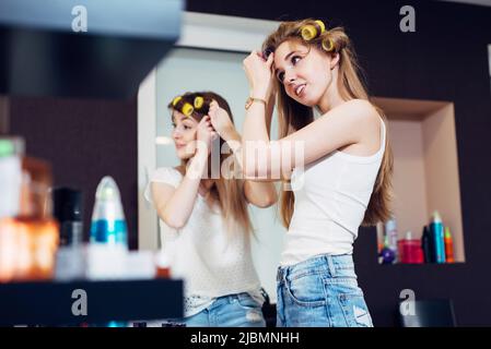 Teenager girls applying hair rollers on their long blond hair preparing to go out. Stock Photo