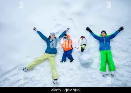 Mother and two boys lay with snowman in snow, top view Stock Photo