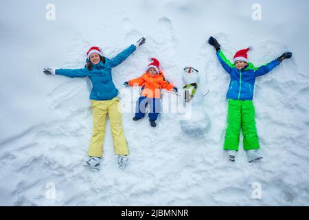 Mother and two boys in Santa hats lay with snowman, top view Stock Photo