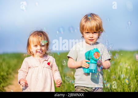 Toddler girl and blond boy brother play with soap bubble gun Stock Photo