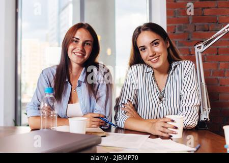 Two young female entrepreneurs sitting at work desk during the business meeting in modern conference room. Stock Photo