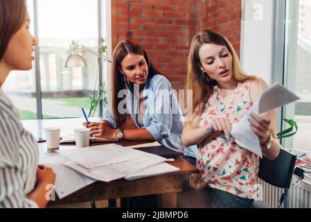 Three female groupmates preparing for exam reading lectures notes sitting at table in a room. Stock Photo