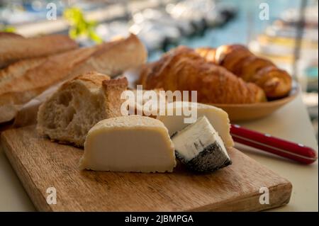 Sunny morning in Provence, breakfast with fresh baked croissant, baquett bread, crottin goat cheese and view on fisherman's boats in harbour of Cassis Stock Photo