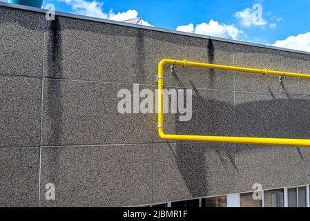A large yellow gas pipe running up a factory wall made of concrete and pebbles. Stock Photo
