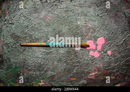 Old brush on paper with dark and silver textured paint with drops of pink acrylic paint Stock Photo