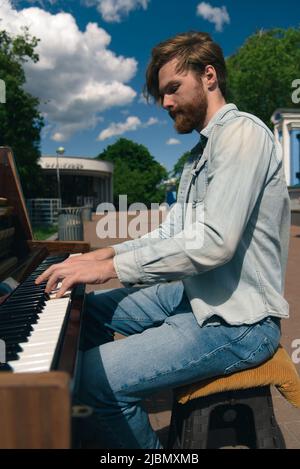 Street musician playing old piano in downtown. Young bearded man pianist playing music outdoors. Handsome talented busker Stock Photo