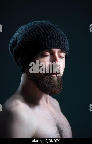 dramatic portrait of a bearded guy in a black knitted hat on a dark background Stock Photo