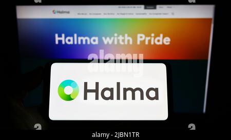 Person holding smartphone with logo of British safety equipment company Halma plc on screen in front of website. Focus on phone display. Stock Photo