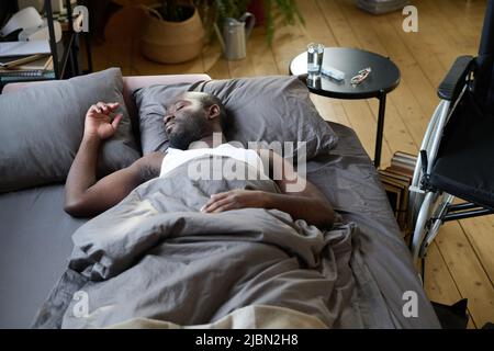 African American man lying on bed under blanket and resting because feeling himself bad Stock Photo