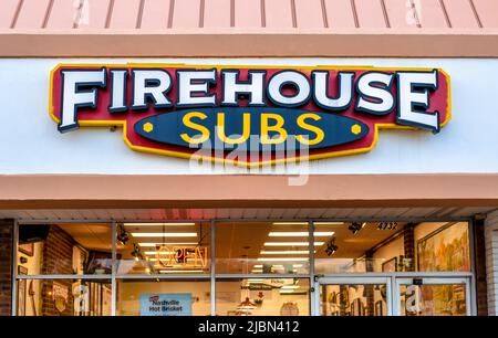 Firehouse Subs exterior facade brand and logo signage above glass windows and doors with lighted interior showing first responder gear decor. Stock Photo