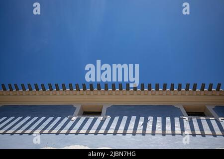 Horizontal photo where you can see the roof of a house with its tiles and the blue facade with two windows. Contrasts with the blue sky. On a tile the Stock Photo