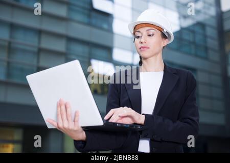 Smiling woman architector in suit and hat is exploring project in her laptop Stock Photo