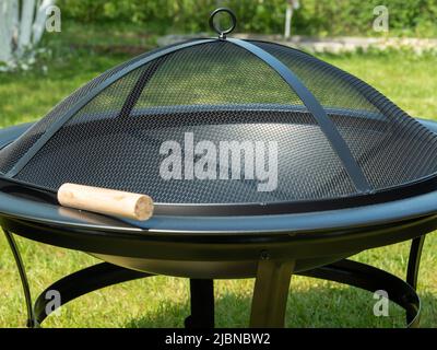 Metal bowl for fire on a background of green grass. Metal fire bowl with lid. Stock Photo