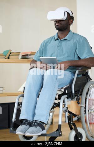 African AMerican man in VR goggles sitting in wheelchair using digital tablet for virtual reality therapy Stock Photo