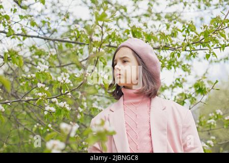 Portrait of little girl stands in a blooming white apple tree in the park. Stock Photo
