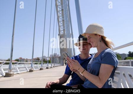 Cheerful mother and son using smartphone on bridge Stock Photo