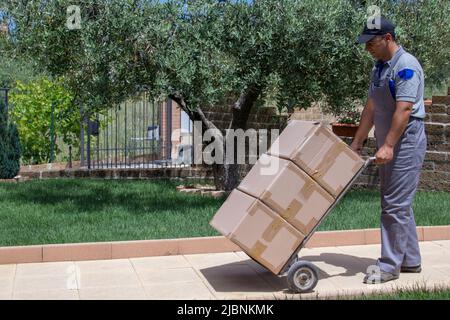 Image of a delivery boy carrying large packages with a trolley at a house Stock Photo