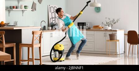 Young man having fun while vacuuming carpet in kitchen Stock Photo
