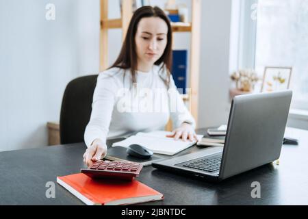 Account balance definition. Female Accountant working with laptop and calculator in office. Stock Photo