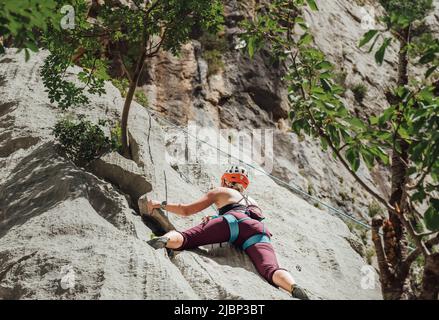 Athletic Woman in protective helmet and shoes climbing on cliff rock wall using top rope and climbing harness in Paklenica National park site in Croat Stock Photo