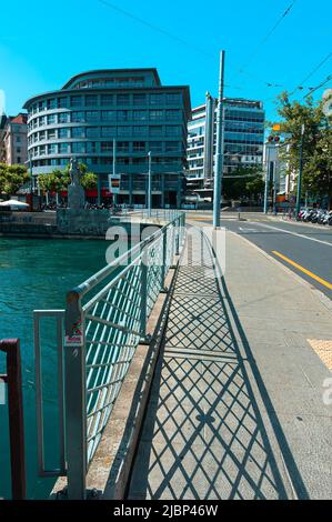 Geneva, Switzerland - June 3, 2022: The buildings in Geneva and the bridge over the Rhone River, reflecting the shadow of the fence Stock Photo