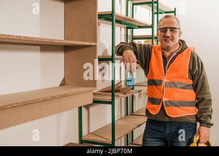 Contractor leaning on the rack after supervising the safety of the construction site and facilities of a store with his hard hat in hand showing joy f Stock Photo