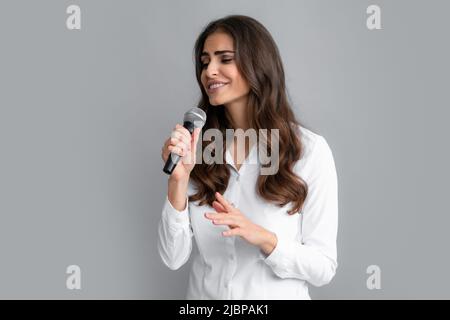 Woman speech, business woman holding a microphone. Stylish girl singing songs with microphone, holding mic at karaoke, posing against gray background. Stock Photo