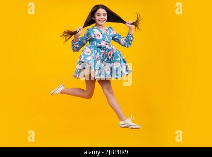 Amazed teenager. Full length overjoyed teenager kid girl 12 13 14 year in casual wear jumping old isolated on yellow background studio. Funny jump Stock Photo