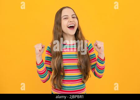 Teenager child overjoyed successful do winner gesture clench fist say yes isolated on yellow background studio. Excited face, cheerful emotions of Stock Photo