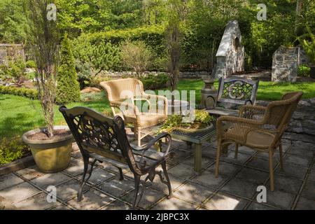 Wrought iron and wooden benches and bonsai tree on coffee table on paving stone patio in backyard garden in spring. Stock Photo