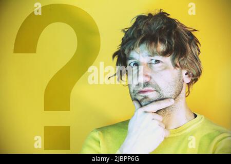 Young man with question mark sign on yellow background Stock Photo